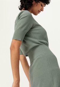 Maglione lavorato a maglia in una tonalità di verde smorzata, con maniche corte, polsini in costina e una silhouette aderente con tessuto testurizzato.
