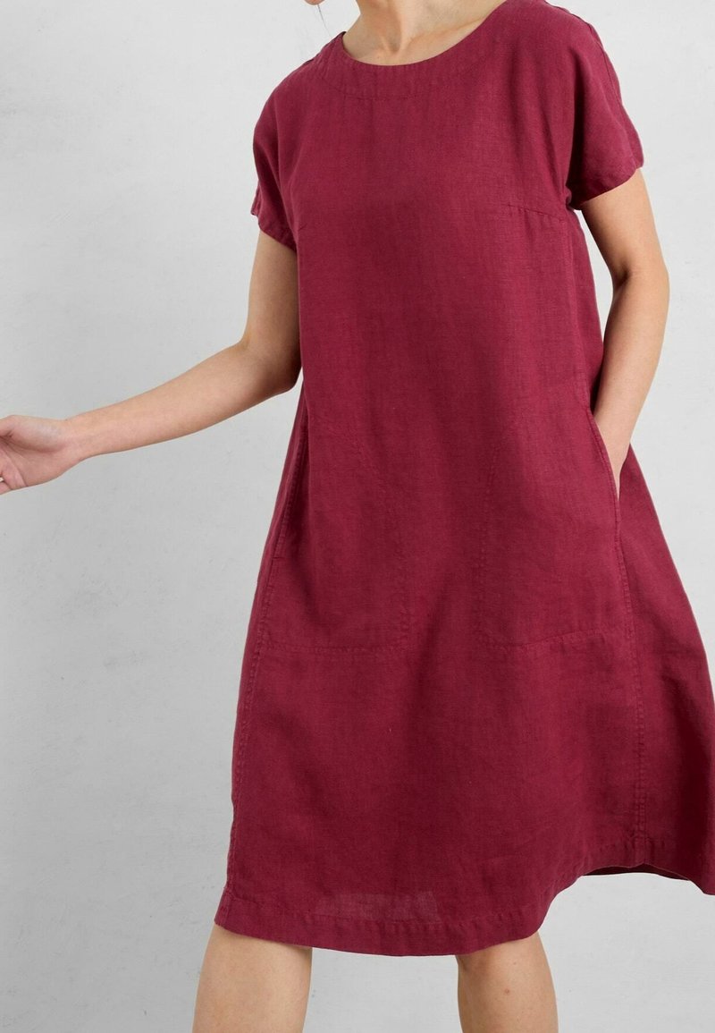 Burgundy linneklänning med korta ärmar, rund halsringning och sidfickor. Flödig silhuett med subtil textur och sömdetaljer.