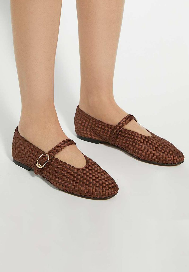 Brown woven flats with a rounded toe and a strap featuring a small metallic buckle. Textured material and flat sole for comfort.