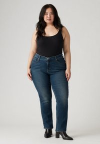 Juodas bakas dėvimas su tiesaus kirpimo mėlynomis džinsomis, turinčiomis klasikinius penkių kišenių dizainą ir siuvinėtus detales, derintas su juodais aukštakulniais auliniais batais.