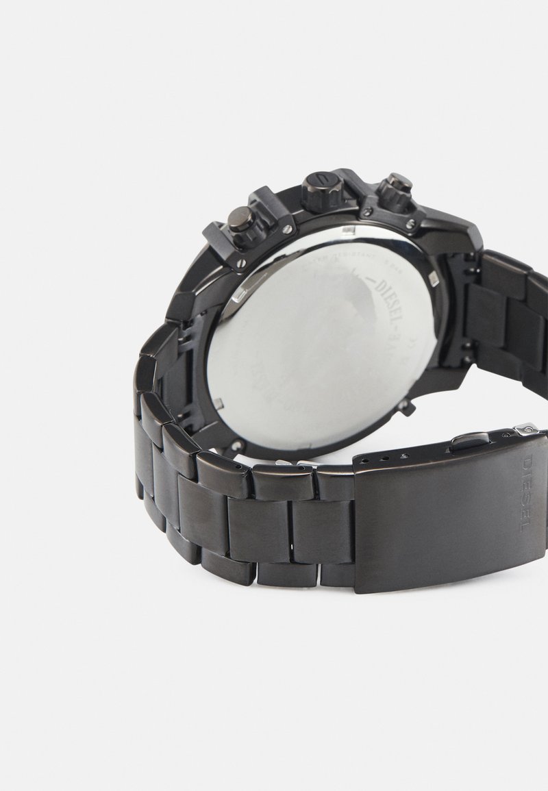 Rückansicht einer schwarzen Metallarmbanduhr mit graviertem Verschluss und sichtbaren Einstelltasten auf weißem Hintergrund.