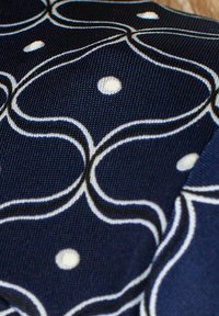 Marinblått tyg med ett vågformat vitt mönster med prickar. Texturen är något grov, med tydlig kontrast mellan färgerna.