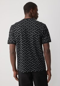 Herret-shirt i sort og grå med et geometrisk zigzag-mønster. Korte ærmer, rund hals, tekstureret design og ensfarvet sort kant.