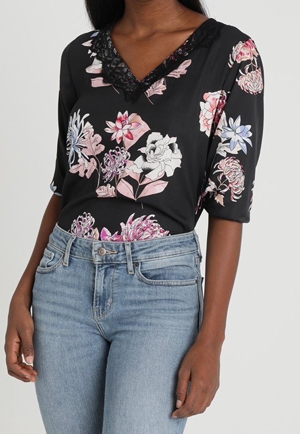 Blouse noire à motif floral avec un col en V bordé de dentelle et des manches à coudes, associée à un jean taille haute bleu clair.