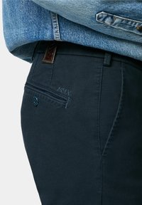 Pantalon texturé bleu marine au design épuré. Comprend une ceinture en cuir tressé marron, une poche latérale et un détail brodé "MMX."