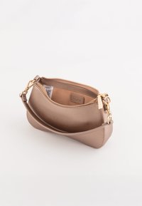 Kleine beige Leder-Handytasche mit goldenem Reißverschluss und Verschluss, teilweise geöffnet, um das Innenetikett und das Pflegeetikett zu zeigen.