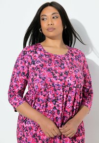 Sukienka w kwiaty w odcieniach różu, fioletu i czerni. Posiada rękawy o długości 3/4, okrągły dekolt oraz marszczoną linię talii.