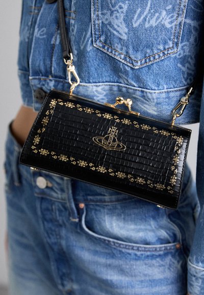 Sac en cuir verni noir avec une texture crocodile, des accents floraux dorés et un logo graphique. Équipé d'une fermeture à clip et d'une bandoulière amovible.
