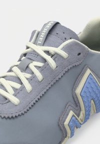 Αθλητικό παπούτσι από ανοιχτό γκρι σουέντ με υφασμάτινες μπλε λεπτομέρειες, λευκά κορδόνια και επένδυση στον αστράγαλο, με λογότυπο στη γλώσσα.