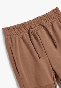 Braune Baumwoll-Jogginghosen mit elastischem Bund, Kordelzug, Seitentasche und gerippten Bündchendetails.