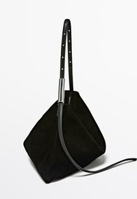 Black suede handbag with a geometric, pyramid shape. Features a detachable black leather strap and a sleek silver connector.