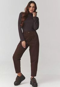 Ciemnobrązowy golf w parze z brązowymi spodniami z wysokim stanem, o luźnym kroju. Czarne buty na platformie dopełniają stylizację.