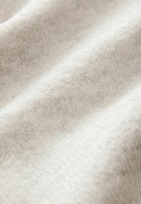 Biała, teksturowana tkanina o miękkim, puszystym wyglądzie z delikatnymi różnicami w odcieniu i cieniowaniu. Idealna na koce lub odzież.