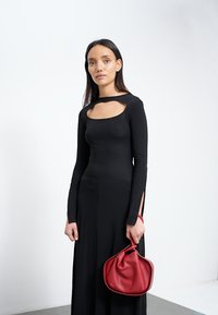 Vestido preto de manga longa com detalhe recortado no peito e fendas laterais; combinado com uma bolsa de couro vermelha com uma forma única.