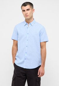 Camisa de manga corta, de color azul claro, con botones, hecha de una tela texturizada, que presenta un cuello apuntado y un logo discreto en el pecho.