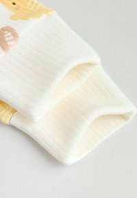 Ribbstickade kragar i gräddfärgat med gul accent; mjuk textur; har lekfulla djurmönster på tyget.