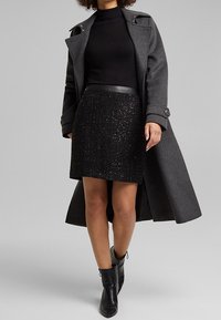 Cappotto in lana grigia con spalle strutturate, dolcevita nero, gonna nera con paillettes e stivaletti. Texture eleganti e finiture contrastanti.