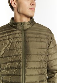 Giacca puffer verde oliva con colletto alto, zip frontale e texture trapuntata orizzontale. Materiale leggero e finitura liscia.