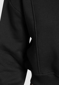 Sweatshirt en coton noir avec une texture lisse, des poignets côtelés et une coupe décontractée. Le design inclut des coutures visibles le long des seams.