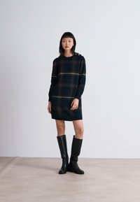 Marinblå rutigt klänning i stickad tyg, med långa ärmar, rundad halsringning och dekorativa axelknappar. Bärs med svarta knä höga stövlar.