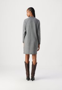 Vestido cinza de manga longa com uma silhueta descontraída, feito de um tecido texturizado. Combinado com botas estilo cowboy castanhas com pontas finas.