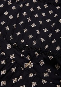 Tissu noir avec un petit motif de diamants blancs et de fleurs, présentant une finition en dentelle et un accent en fermeture éclair dorée près de l'ourlet.