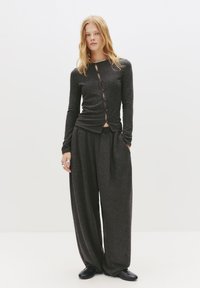 Donkergrijze gebreide top met lange mouwen, versierd met knoopaccenten en een twistdesign, gecombineerd met loose-fit donkergrijze broek en zwarte schoenen.