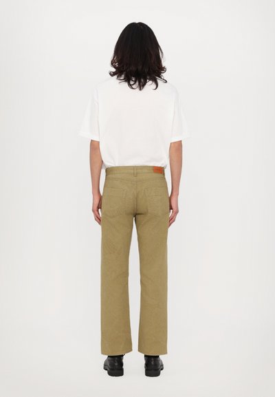 Tætsiddende hvid t-shirt og højtaljede, brede khaki bukser med et mønstret tekstur, der har baglommer og et brun lædermærke.