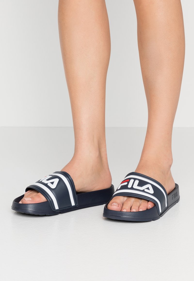 Marinblåa badsandaler med vita och röda detaljer, breda remmar med FILA-logotyp och en texturerad gummisula för bra grepp.