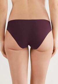 Burgundy bikiniunderdel med en slät, matt textur och en låg midja, med högskurna ben och minimal täckning bak.