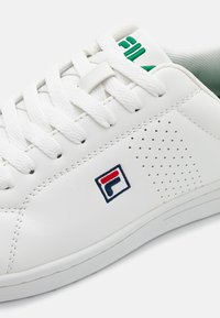 Sneaker bianco in pelle con punta rotonda, dettagli perforati, lacci piatti e un logo con accenti rossi e blu. Fodera interna verde.