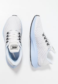 Scarpe da corsa Nike in mesh grigio chiaro con dettagli neri, colletto imbottito e suola in gomma blu morbida. Presentano un design traspirante.