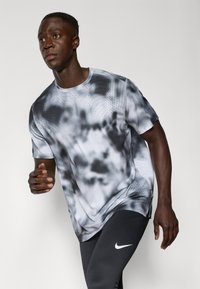 Athletic shirt in gray with a tie-dye pattern and perforated detailing, made from moisture-wicking fabric. Short sleeves and crew neck design.