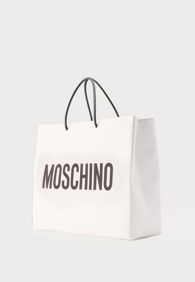 Sac de shopping Moschino blanc avec des poignées noires et le nom de la marque en lettres noires et épaisses à l'avant, posé sur un fond clair uni.