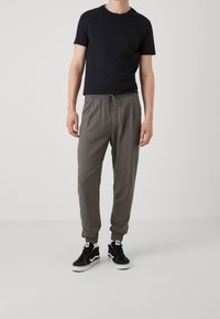 Svart t-shirt med rund hals, ljusgrå byxor med elastiskt midjeband och svarta sneakers med vit sula. Byxorna har manschetter vid anklarna.
