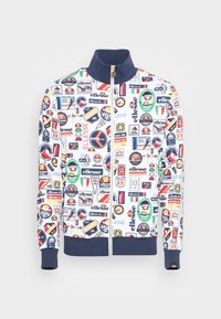 Vit zip-up jacka med olika färgglada logopatchar. Den har en marinblå krage och muddar, med en jämn tygtextur genom hela jackan.