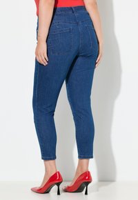 Úzké džíny v tmavě modrém denimu s vysokým pasem, vybavené zadními kapsami a hladkou texturou, doplněné červenými lodičkami na vysokém podpatku.