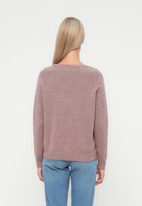 Staubrosa Strickpullover mit langen Ärmeln, rundem Ausschnitt und geripptem Saum, kombiniert mit hellblauen Jeans, von hinten gesehen.