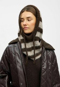 Brun quiltet jakke over en mørk sweater, prydet med et stribet uldscarf i brun og grå med to hængende bånd.