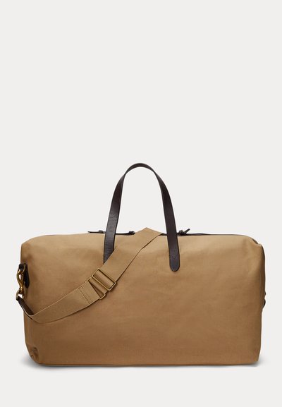 Large rectangular tan canvas duffel bag with dark brown leather handles and adjustable shoulder strap with brass hardware, on white background.