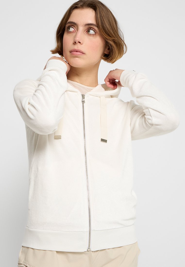 Felpa bianca con zip in morbido materiale, dotata di cappuccio foderato, lacci e dettagli in argento. Tessuto liscio con polsini e orlo a costine.