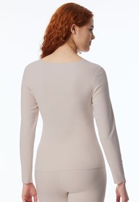 Langarmshirt in hellbeige mit rundem Ausschnitt und taillierter Passform. Der Stoff wirkt glatt und elastisch, ideal zum Layering.