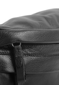 Borsa in pelle nera con una soffice texture, dotata di chiusura lampo e dettagli cuciti lungo il bordo. Con una forma a testa arrotondata.