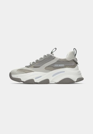 Kenkät, joissa on paksut harmaat ja valkoiset sävyt, verkkopaneelit, paksu muotoiltu pohja, nauhat, vetotapit kannassa ja kielekkeessä sekä "Steve Madden" -logo sivussa.