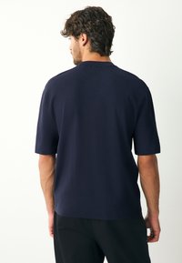 Tumši zils īsroku adīts krekls ar brīvu pieguli, fakturētu audumu un apaļu kakla izgriezumu. Izstrādāts bez pamanāmiem rotājumiem.