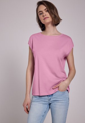 Korte mouwen roze t-shirt van zachte stof, met een ronde halslijn en een ontspannen pasvorm. Gepaard met lichtblauwe jeans.