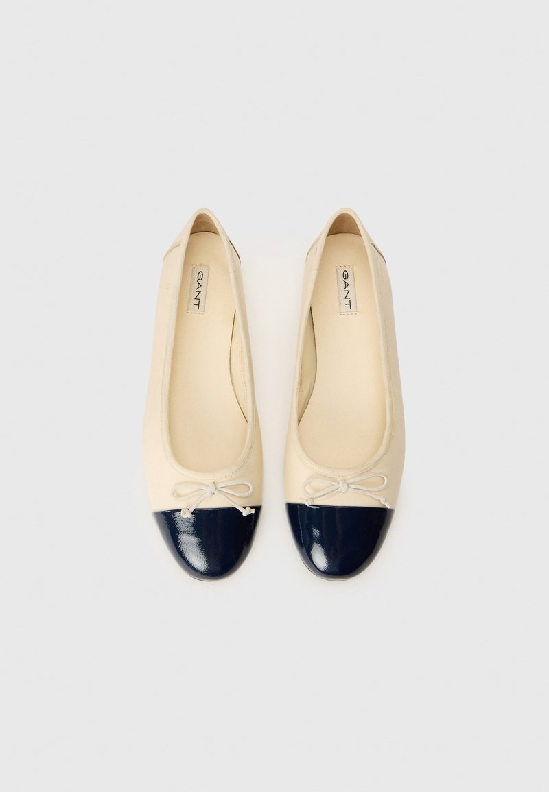 Ballerines beiges avec des embouts brillants navy et de petits nœuds à l'avant, marquées "GANT" sur la semelle intérieure.