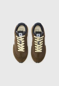 Brown suede and mesh sneakers with cream laces, grey accents, and black rubber sole. Features a prominent logo on the tongue.
