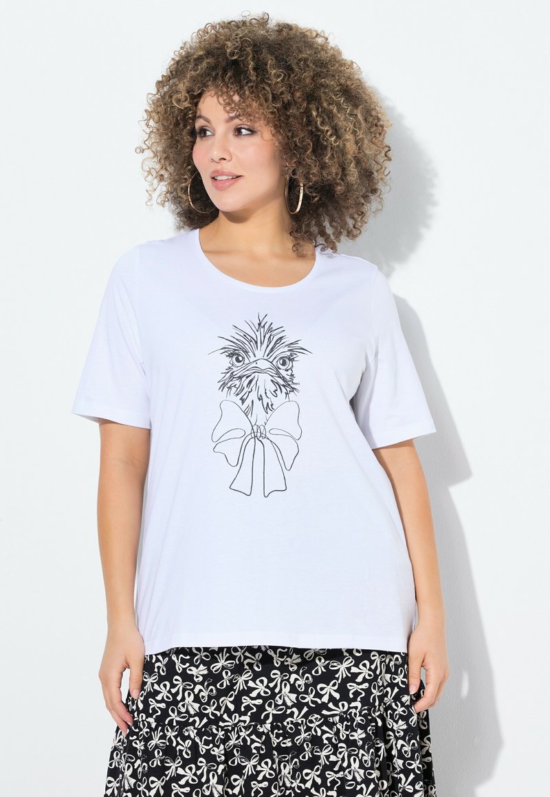 Camiseta blanca de algodón con una ilustración de contorno negro de un pájaro que lleva un lazo. Combinada con una falda negra con patrones de lazos blancos.