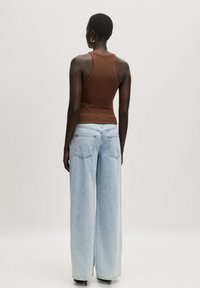 Bruine geribbelde tanktop gecombineerd met lichtblauwe wijde jeans. De outfit heeft een aansluitende silhouet met een zachte textuur en een casual ontwerp.